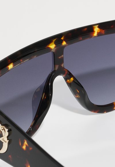 Lunettes de soleil en écaille de tortue avec des verres dégradés foncés. Dotées d'un cadre audacieux et épais avec une finition brillante et un logo subtil sur le côté.