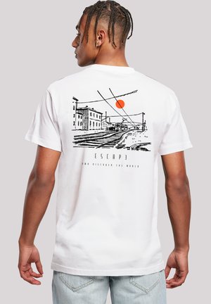 Mann mit geflochtenem Haar, der ein weißes T-Shirt mit schwarzem Sketch von Eisenbahnschienen, Gebäuden und einer orangefarbenen Sonne auf dem Rücken trägt.