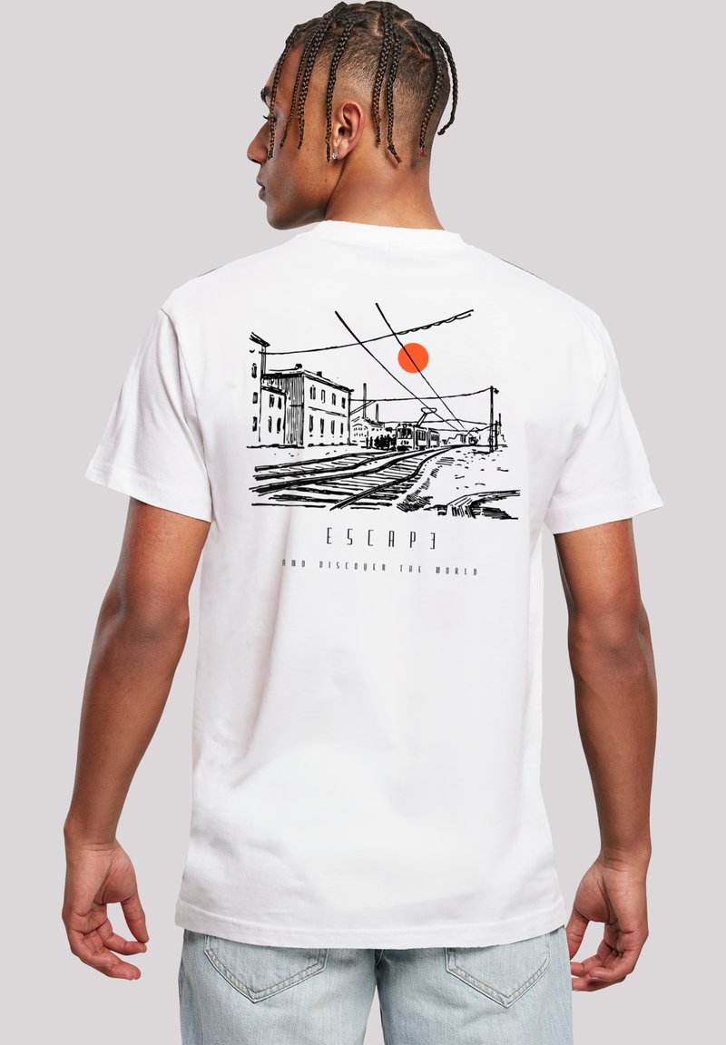 Mann mit geflochtenem Haar, der ein weißes T-Shirt mit schwarzem Sketch von Eisenbahnschienen, Gebäuden und einer orangefarbenen Sonne auf dem Rücken trägt.