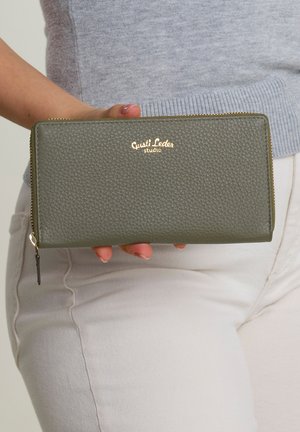 Green leather wallet with a textured finish, gold logo accent, and zip closure. Held in hand, featuring a rectangular shape.