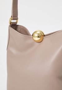 Borsa a spalla in pelle beige con una texture liscia e chiusura circolare in metallo dorato con il logo "Furla" impresso. Cintura regolabile attaccata.