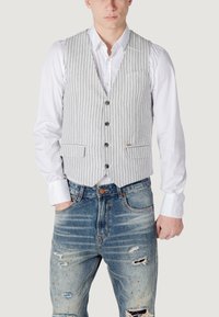 Gilet a righe grigie e bianche con scollatura a V, cinque bottoni e tasche laterali, abbinato a jeans blu scavati con strappi e lavaggio chiaro.