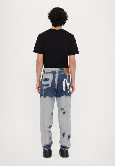 Jean en denim présentant un dégradé de bleu délavé à gris clair, des détails effilochés et une étiquette en cuir marron dans le dos de la taille.
