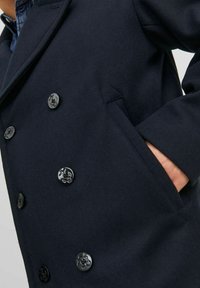 Cappotto doppiopetto blu navy realizzato in misto lana, con grandi bottoni neri, tasche laterali e un design strutturato.