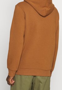 Felpa cappuccio marrone con polsini e orlo a coste. Realizzata in un morbido tessuto texturizzato. Design semplice senza loghi o motivi visibili.