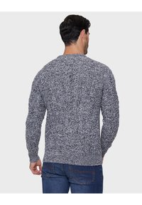 Svetr pletený v mramorovém šedém a černém vzoru, kulatý výstřih, texturovaná tkanina, dlouhé rukávy a žebrovaný lem, nošený s modrými jeansy.