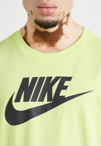 Camiseta de algodón verde lima con gran logo negro de "NIKE" y swoosh. Presenta un cuello redondo y una textura de tela suave.