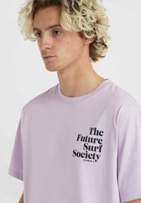 Vaaleanlila t-paita pehmeää puuvillaa, jossa on musta graafinen tekstisuunnittelu edessä, joka lukee "The Future Surf Society" O'Neillin toimesta.