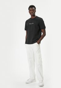 Sort kortærmet sweatshirt med "amour" broderet i hvid, parret med hvide cargo-bukser og hvide sneakers.