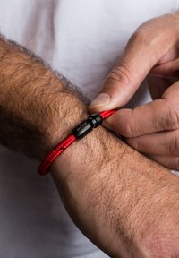 Raudona pintinė apyrankė su juodu užsegimu, pasižyminti lygiu paviršiumi ir tvirtu prigludimu prie riešo.
