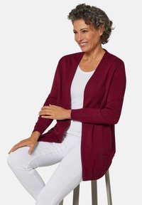 Bordeaux cardigan met open voorkant, lange mouwen en zijzakken. Zacht breiwerk materiaal gecombineerd met een witte top en witte broek.