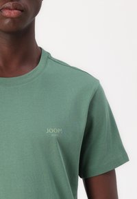 Zöld pamut póló kerek nyakkal, kicsi sárga "JOOP! JEANS" logóval a mellkasán. Rövid ujjú, sima tapintású.