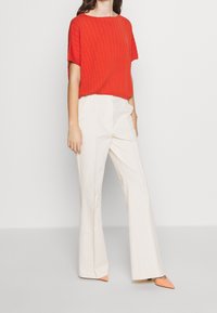 Top corto de rayas rojas con manga corta combinado con pantalones de campana blancos de cintura alta y zapatos de punta naranja, mostrando un diseño texturizado.