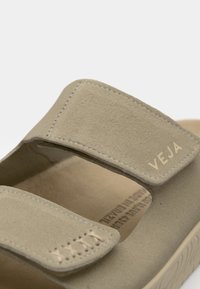 Bež sueded sandale s dva podesiva čičak remena, teksturiranim uloškom i urezanim "VEJA" logom na gornjem remenu.