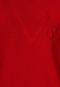 Maglione rosso con design testurizzato, con "1969" e "V" in rilievo sul davanti. Tessuto liscio con un colore e una finitura uniformi.