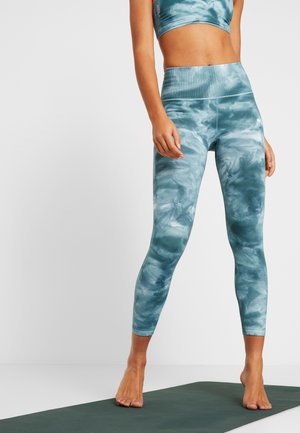 Leggings marbrés bleus et verts avec une taille haute côtelée, présentant un design ajusté et un tissu doux et extensible. Portés avec un crop top assorti.