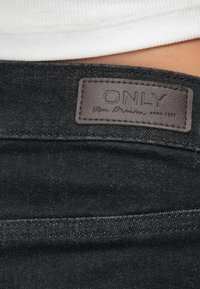 Černé denimové džíny s hladkou strukturou, které mají na pase přišitou hnědou koženou etiketu s názvem "ONLY Blue Denim".