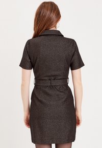 Robe noire à manches courtes avec col, présentant un motif texturé et une ceinture à la taille. La conception est cintrée, se terminant au-dessus du genou.