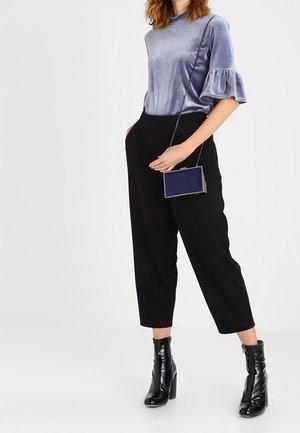 Haut en velours, à manches courtes, bleu clair avec des poignets volantés, associé à un pantalon noir taille haute et fuselé et des bottines noires vernies.