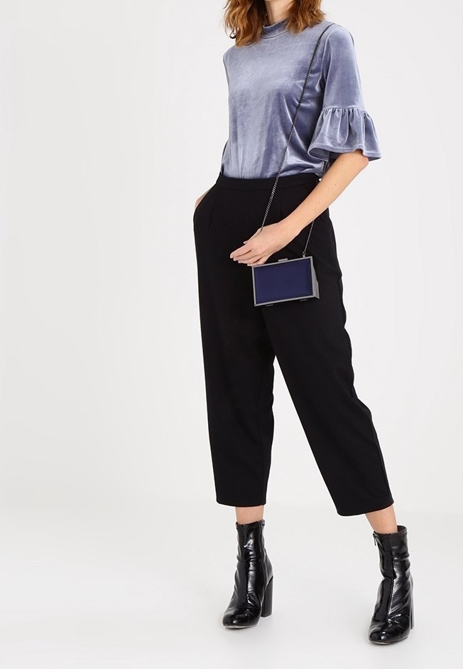 Haut en velours, à manches courtes, bleu clair avec des poignets volantés, associé à un pantalon noir taille haute et fuselé et des bottines noires vernies.