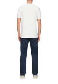 T-shirt en coton blanc à manches courtes, associé à un jean en denim bleu foncé. Le jean présente une coupe droite classique et des poches arrière.