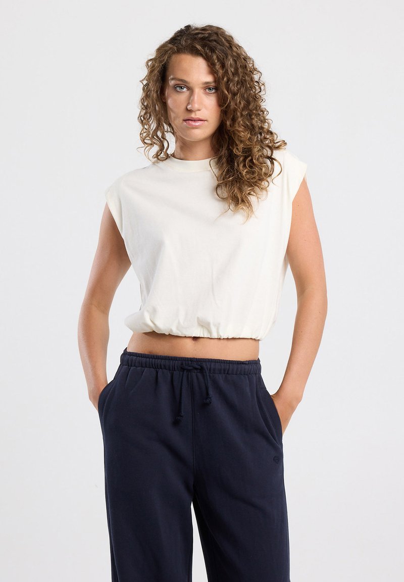 Cream sleeveless top with a cinched hem, made of soft cotton; paired with navy jogger pants featuring an elastic waistband and side pockets.
