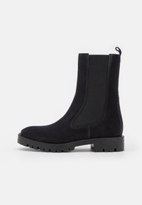 Black suede Chelsea boot with chunky lug sole, elastic side panel, and pull tab on plain white background.