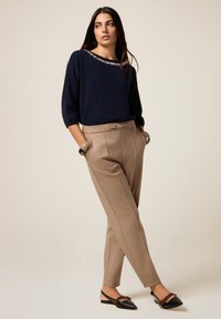 Pull marin avec un col décoré, pantalon beige cintré et ballerines noires à talon avec des accents marron. Textures lisses, coupe décontractée.