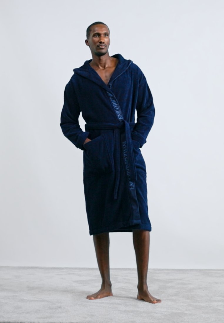 Peignoir à capuche bleu marine en tissu doux et texturé, doté d'une ceinture nouée à la taille et de poches latérales. Marquage brodé sur le devant.