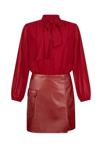 Blusa rossa con scollatura a fiocco e chiusura frontale con bottoni. Abbinata a una mini gonna in pelle rossa con tasca laterale e texture liscia.