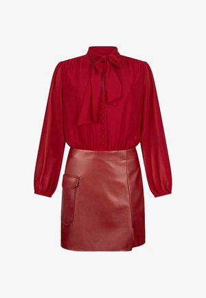 Blusa rossa con scollatura a fiocco e chiusura frontale con bottoni. Abbinata a una mini gonna in pelle rossa con tasca laterale e texture liscia.