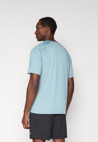 Ανοιχτό μπλε αθλητικό κοντομάνικο με στρογγυλή λαιμόκοψη και επίπεδες ραφές, συνδυασμένο με σκούρα σορτς που φέρουν λογότυπο στο τελείωμα.