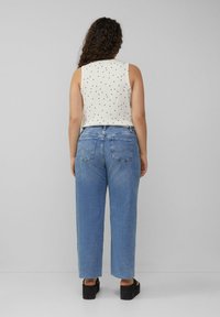 Wit mouwloos topje met zwarte stippen, gecombineerd met lichtblauwe wijde jeans. Zwarte platform sandalen maken de outfit af.