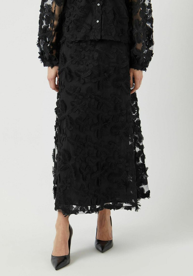 Svart brodert todelt sett med en gjennomsiktig topp med langermet og en matchende skjørt med blomsterutskrifter og frynse detaljer.