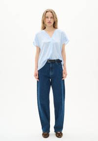 Blusa blu chiaro a maniche corte con scollatura a V abbinata a jeans blu scuro a vita alta e gamba dritta, accompagnata da scarpe ballerine con stampa leopardo.