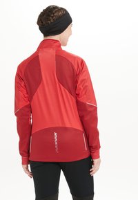 Röd atletisk jacka med en strukturerad design, som har en blandning av släta och texturerade material, reflektiv detaljer och en hög krage.
