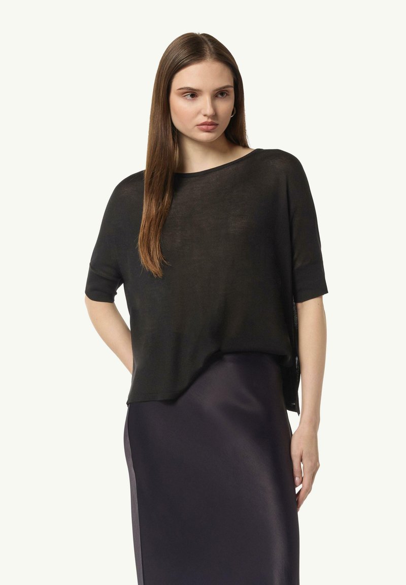 Czarna, luźna dzianinowa bluzka z krótkimi rękawami i szerokim dekoltem, noszona na ciemnej satynowej spódnicy o lekko przezroczystej fakturze.