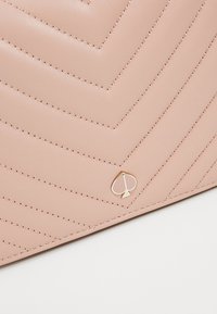 Borsa a tracolla in pelle rosa chiaro con trapuntatura a zigzag, dotata di hardware dorato e piccolo logo a forma di paletta. Texture liscia e dettagli cuciti.