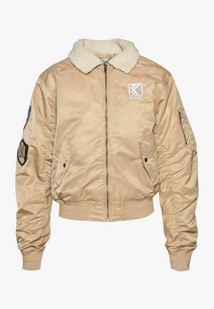 Beež bomber-jakk, millel on faux karusnahast krae, elastsed mansetid ja vöökoht. Omab logo õmblust ja küljetaskuid kasutusmugavuse jaoks.