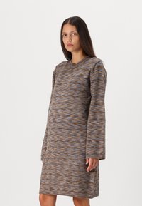 Robe de longueur genou à col rond, marron avec des motifs texturés bleus et oranges. Manches longues, tissu en tricot doux, fentes sur les côtés.