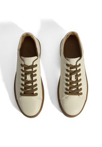 Cremefarbene Ledersneakers mit braunen Schnürsenkeln, runder Zehenform und hellbrauner Gummisohle. Glatte Textur mit dezenten Nähten.