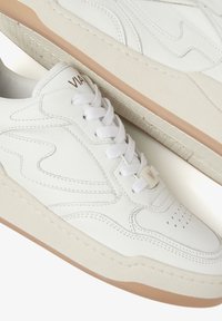 Weiße Leder-Sneaker mit perforierter Zehe, strukturierten Seiten und beigefarbenem Gummiaußensohle. Mit weißen Schnürsenkeln und Logo-Akzent auf der Zunge.