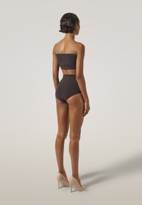 Top bikini nero senza spalline e slip a vita alta. Texture liscia. La modella indossa tacchi alti color beige, vista da dietro.