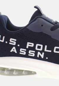 Mornarska športna obutev z belim napisom "U.S. POLO ASSN.". Ima mrežasto zgornji del, oblazinjen ovratnik in vidno zračno blaženje v podplatu.