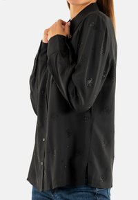 Blusa nera con maniche lunghe, colletto e dettagli sottili. Tessuto morbido con una consistenza liscia e bottoni sul davanti.