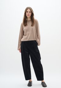 Maglietta beige chiaro a maniche lunghe, taglio rilassato, con una trama sottile. Abbinata a pantaloni in corduroy neri a vita alta, caratterizzati da un design a gamba ampia.