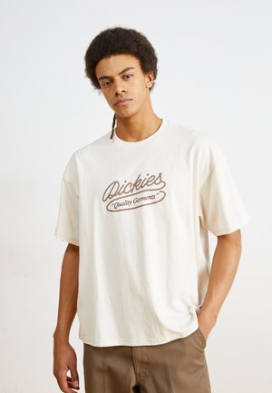 T-shirt oversize color crema in cotone, con un logo ricamato marrone "Dickies Quality Garments" sul petto.