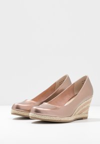Tacchi a cuneo metallici color oro rosa con punta arrotondata e una piattaforma in juta intrecciata. Texture liscia con un leggero luccichio e forma uniforme.