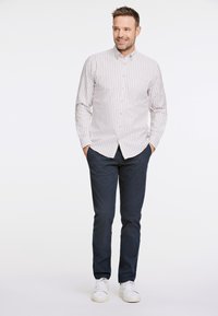 Camisa de botones a rayas en beige claro y blanco, combinada con pantalones azul oscuro y zapatillas blancas. Presenta un cuello y un bolsillo frontal.