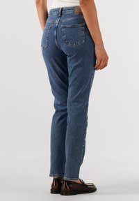 Hög midja, rak ben blå denimjeans med medeltvätt, som har två bakfickor och en läderpatch vid midjan.
